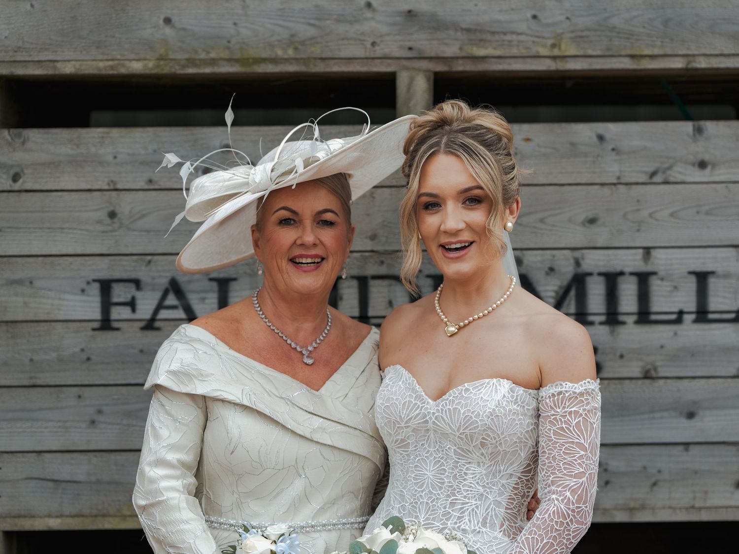 Two people wearing elegant cream-colored formal attire pose together at Falside Mill.