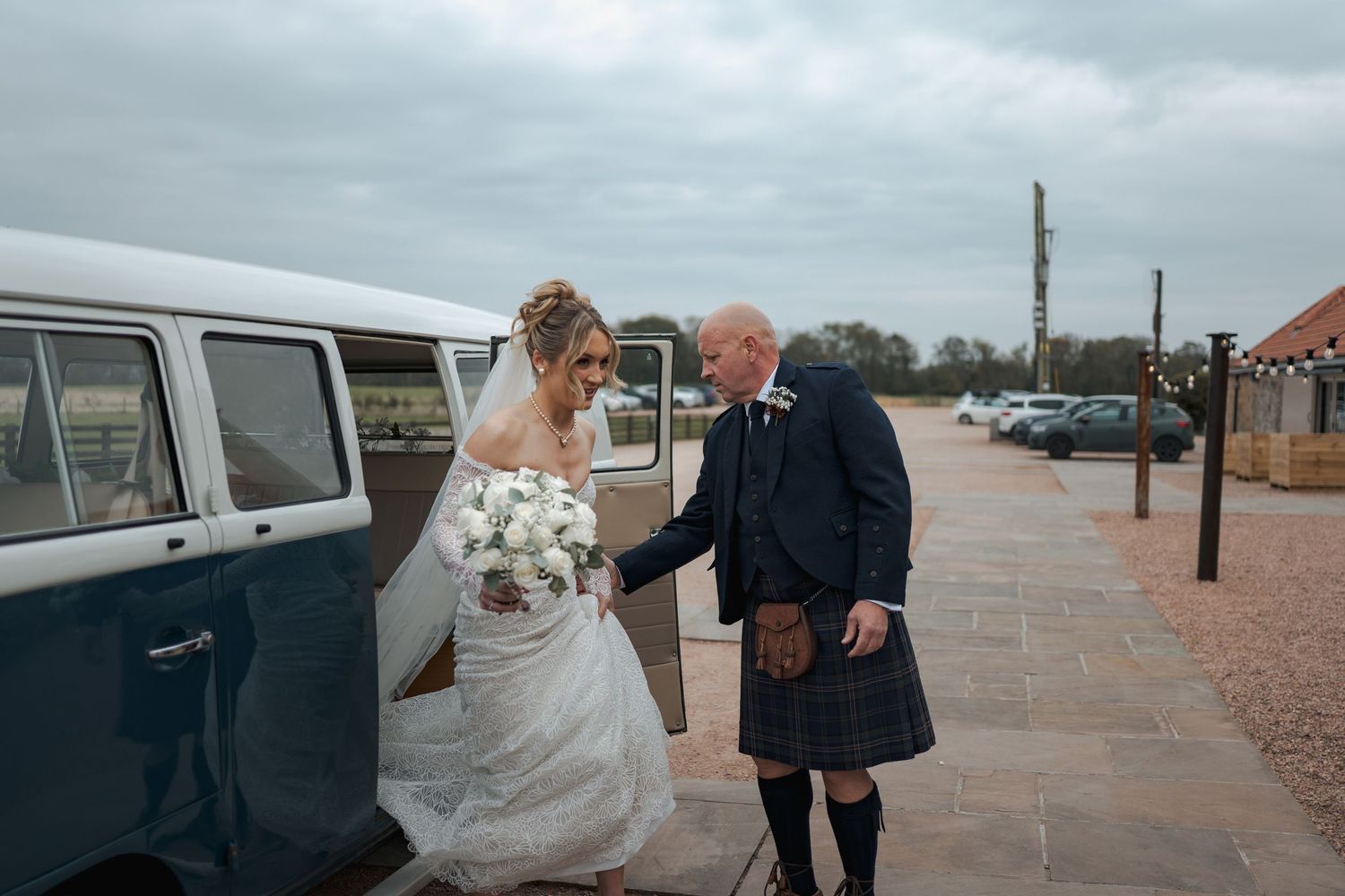 A couple walking along a scenic waterfront boardwalk in formal wedding attire on a cloudy day.
