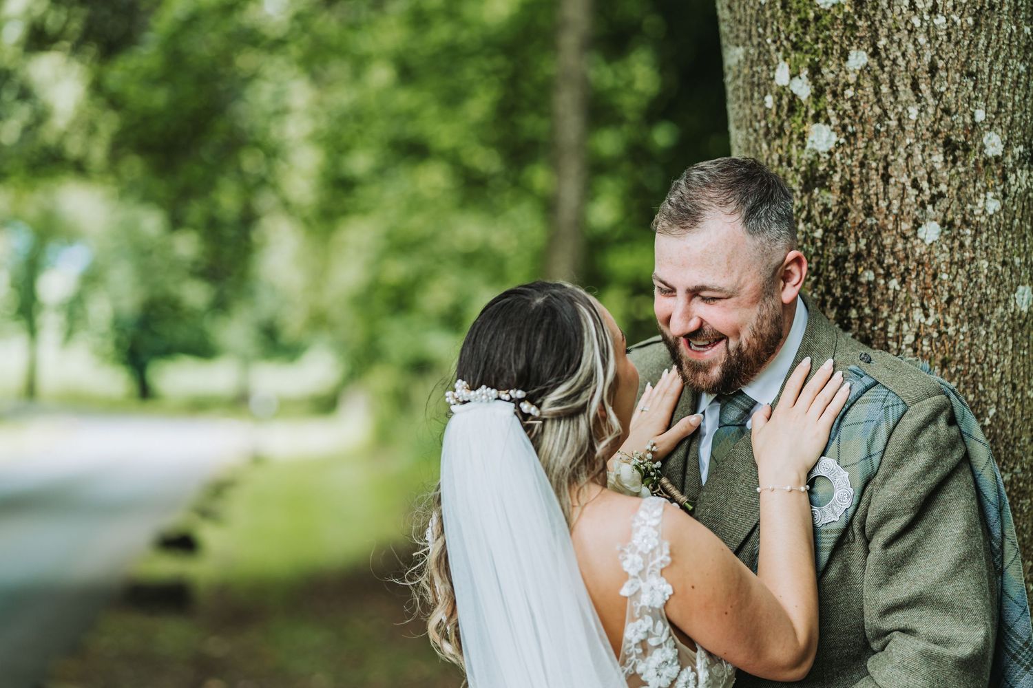 Joyful wedding couple share intimate moment against tree trunk in outdoor setting at Cornhill Castle.