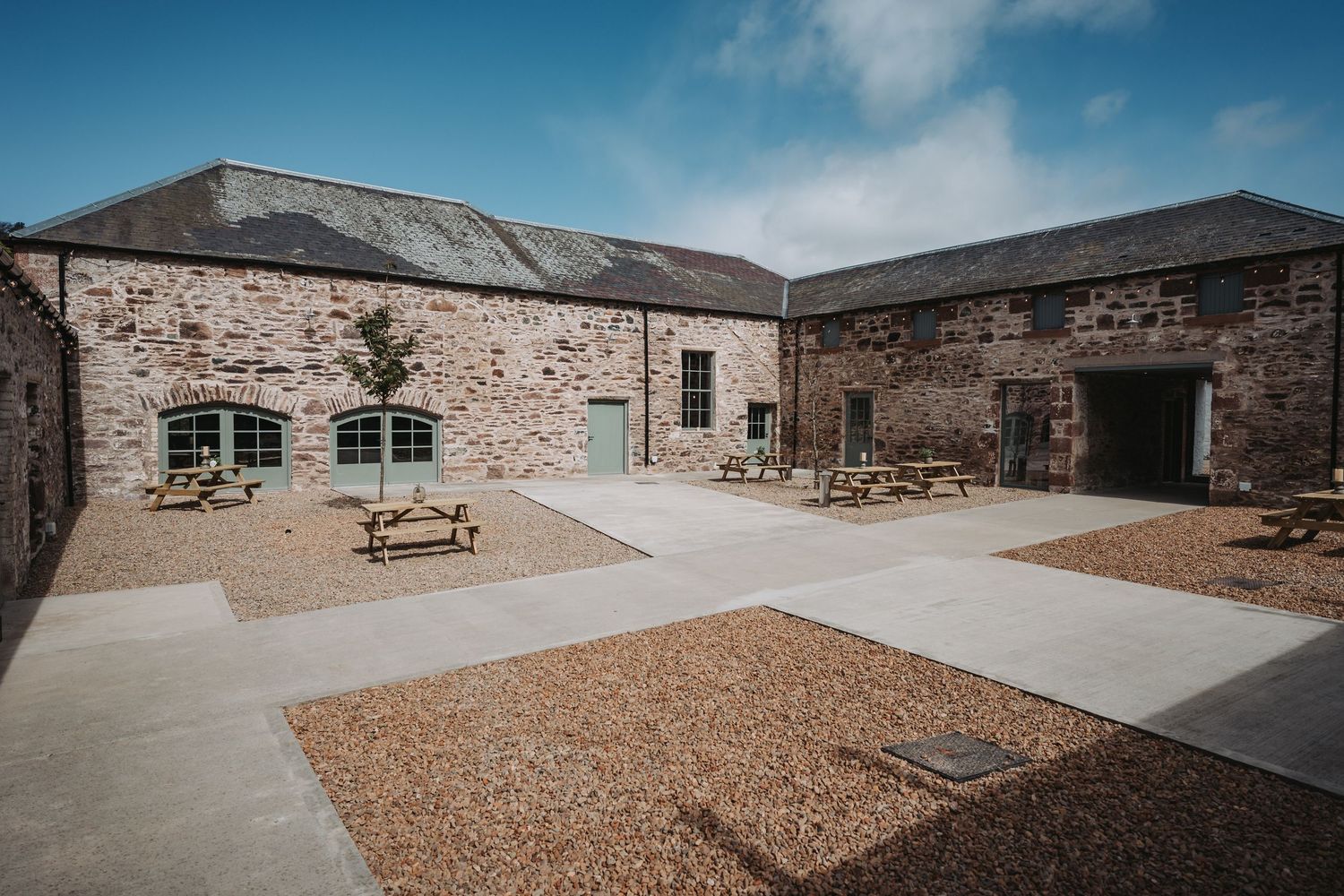 Modern stone courtyard at Kinclune Steading with picnic tables and geometric paving design at converted historic building complex.