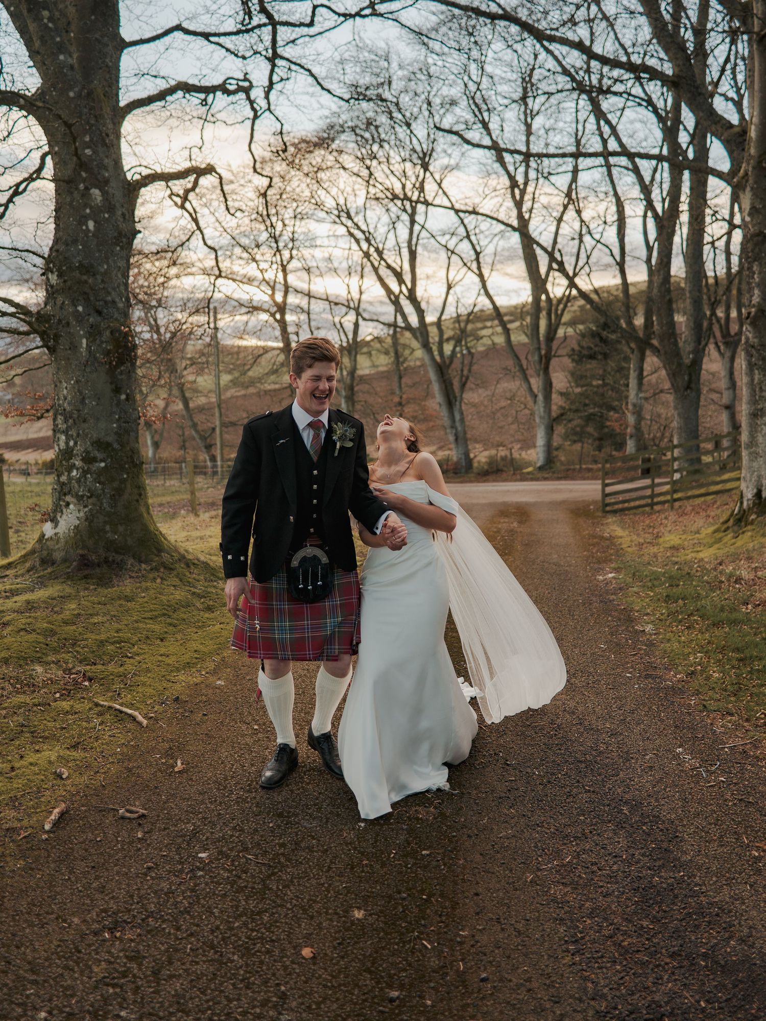 Bride and groom walking hand in hand on a woodland path, groom wearing a traditional Scottish kilt at a outdoor wedding.