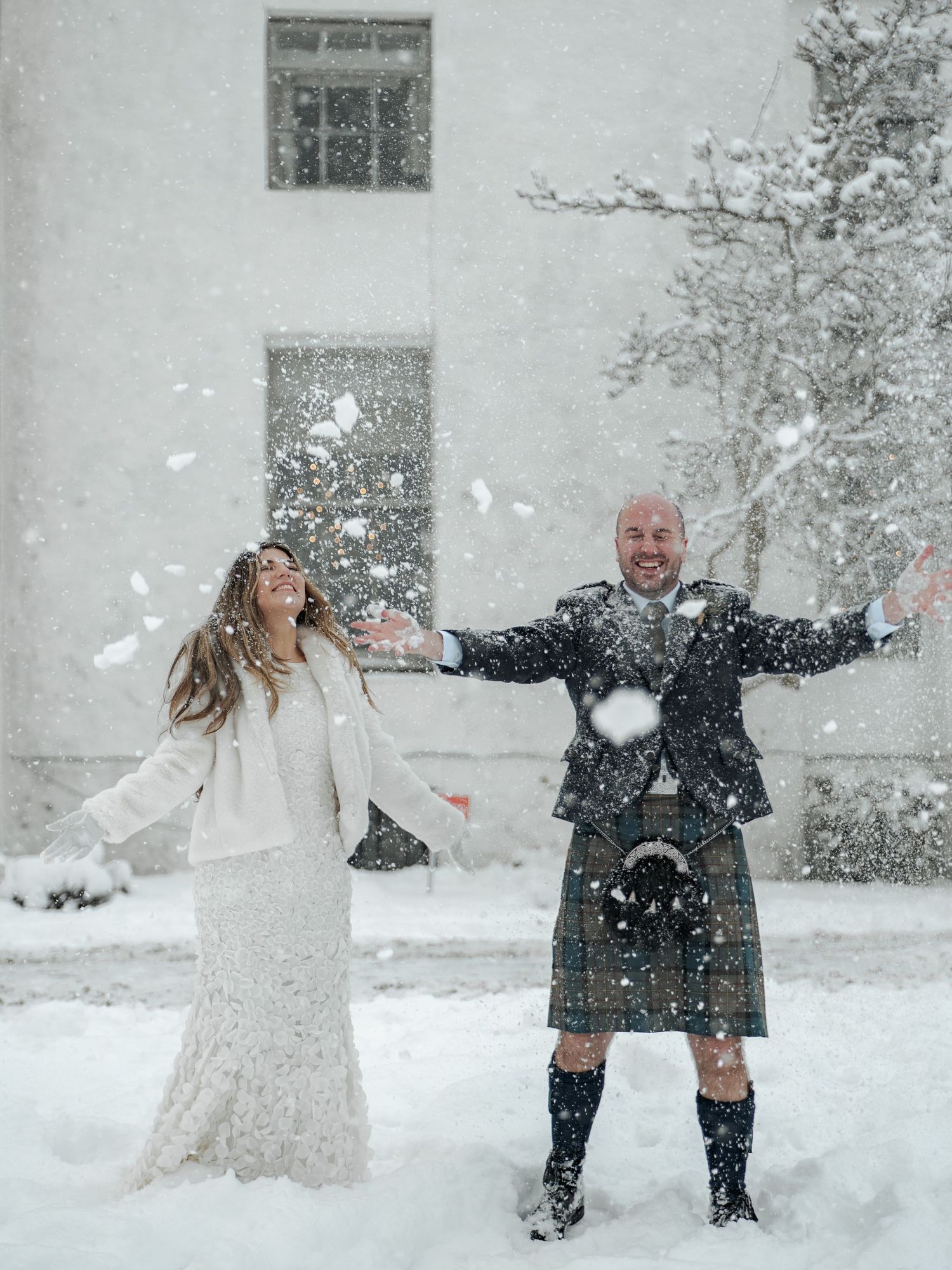 A couple in winter attire plays joyfully in the snow during a romantic outdoor photo session.