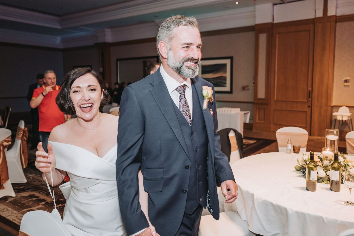 Wedding celebration shows couple entering reception room with joyous expressions as guests look on.