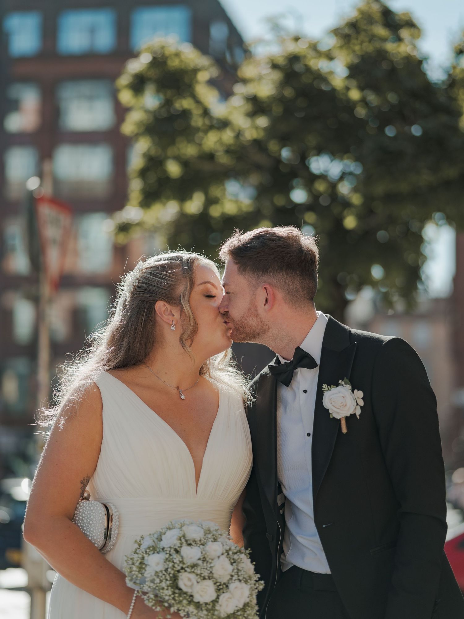 A romantic wedding couple shares tender kisses in a series of candid outdoor portraits with brick buildings in the background.