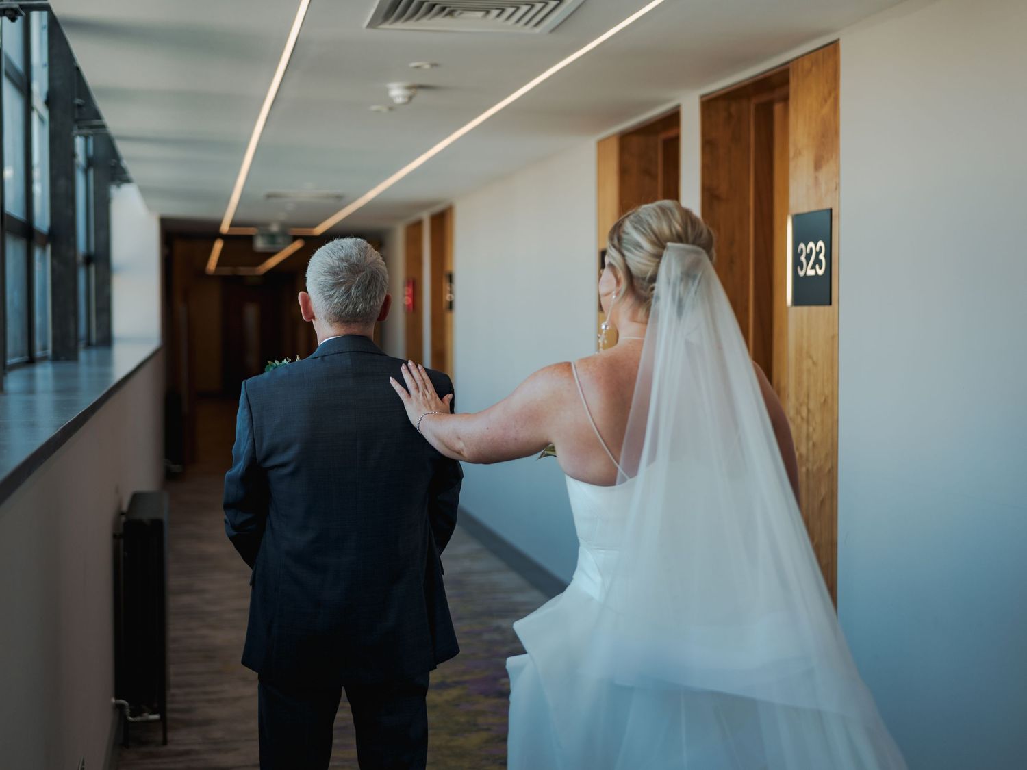 A bride and groom stand in a modern hallway during their first look wedding moment.