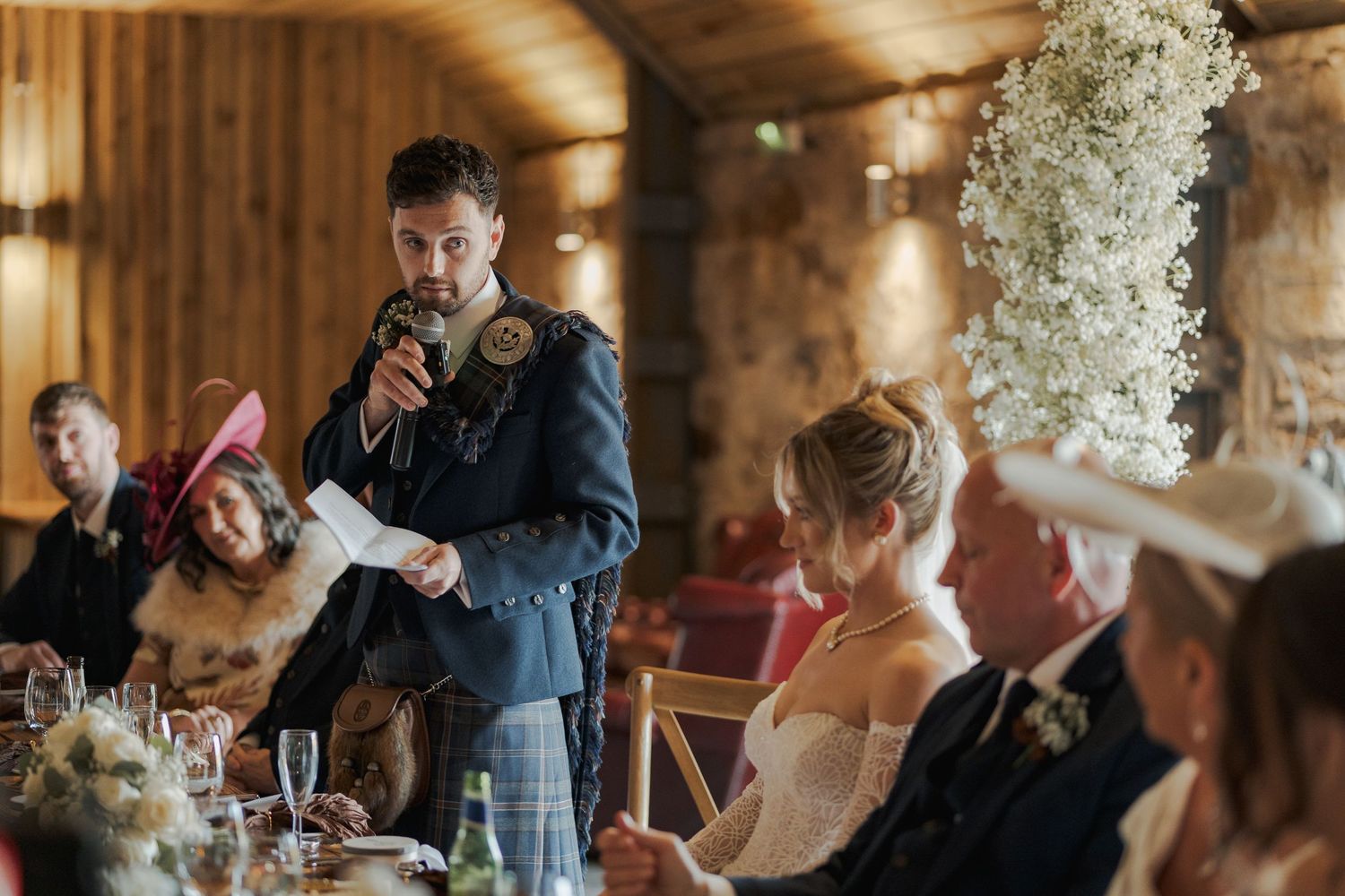 Guests enjoying a celebratory moment at an elegant wedding reception at Falside Mill with floral centerpieces.