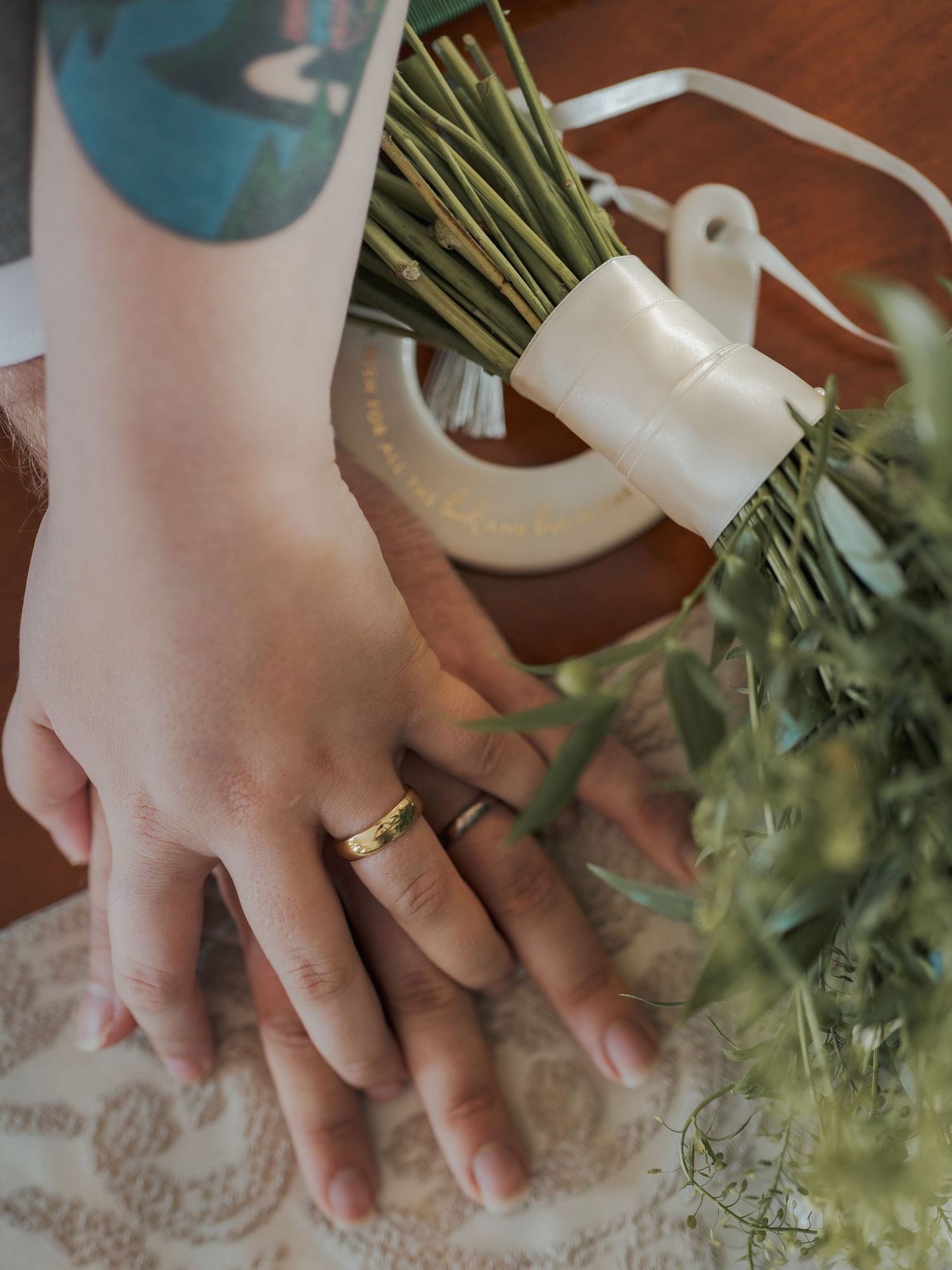 A hand wearing a gold ring arranges fresh parsley stems against a decorated wooden table backdrop.