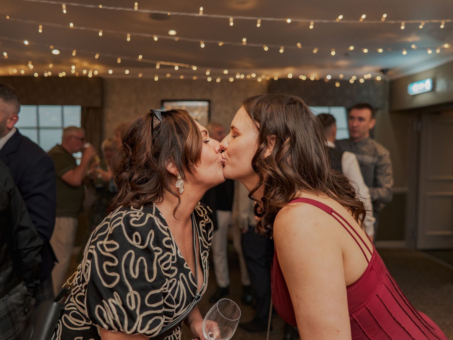 Wedding reception guests dancing and celebrating under warm string lights at an indoor venue.