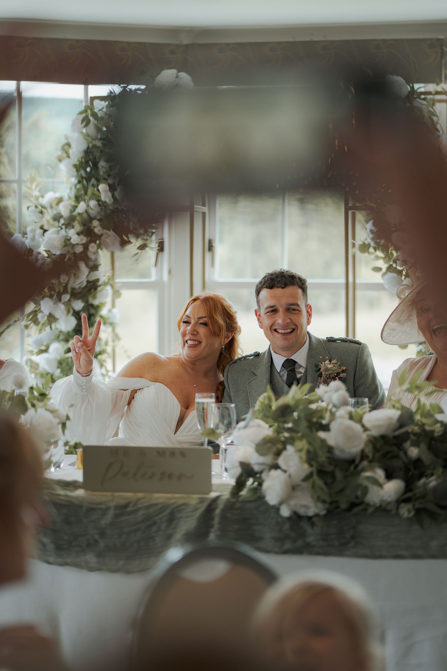 Wedding reception dinner features intimate candlelit table with white floral arrangements under soft window lighting.