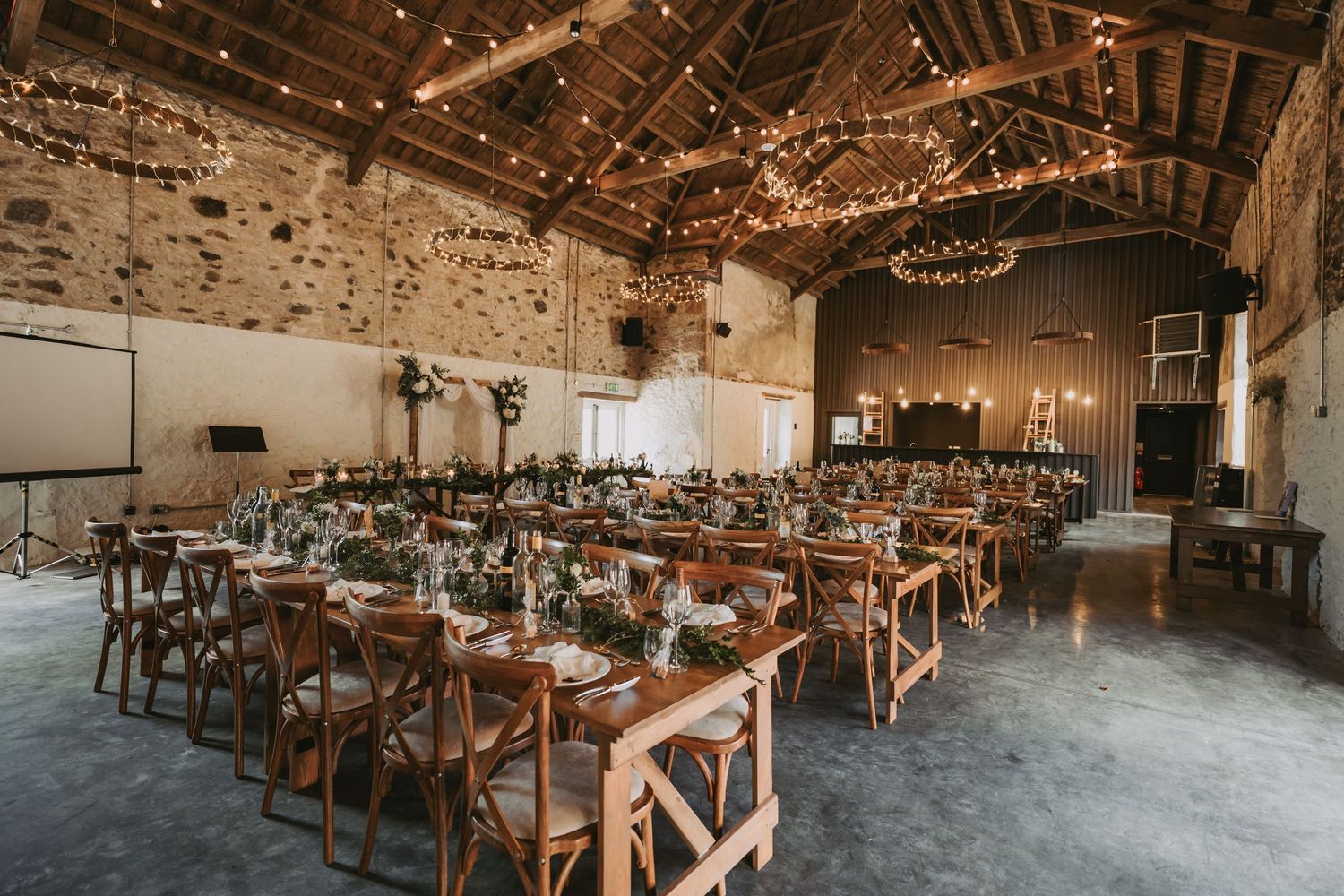 Rustic barn wedding reception venue Kinclune House with wooden cross-back chairs and string lights hanging from exposed beams.