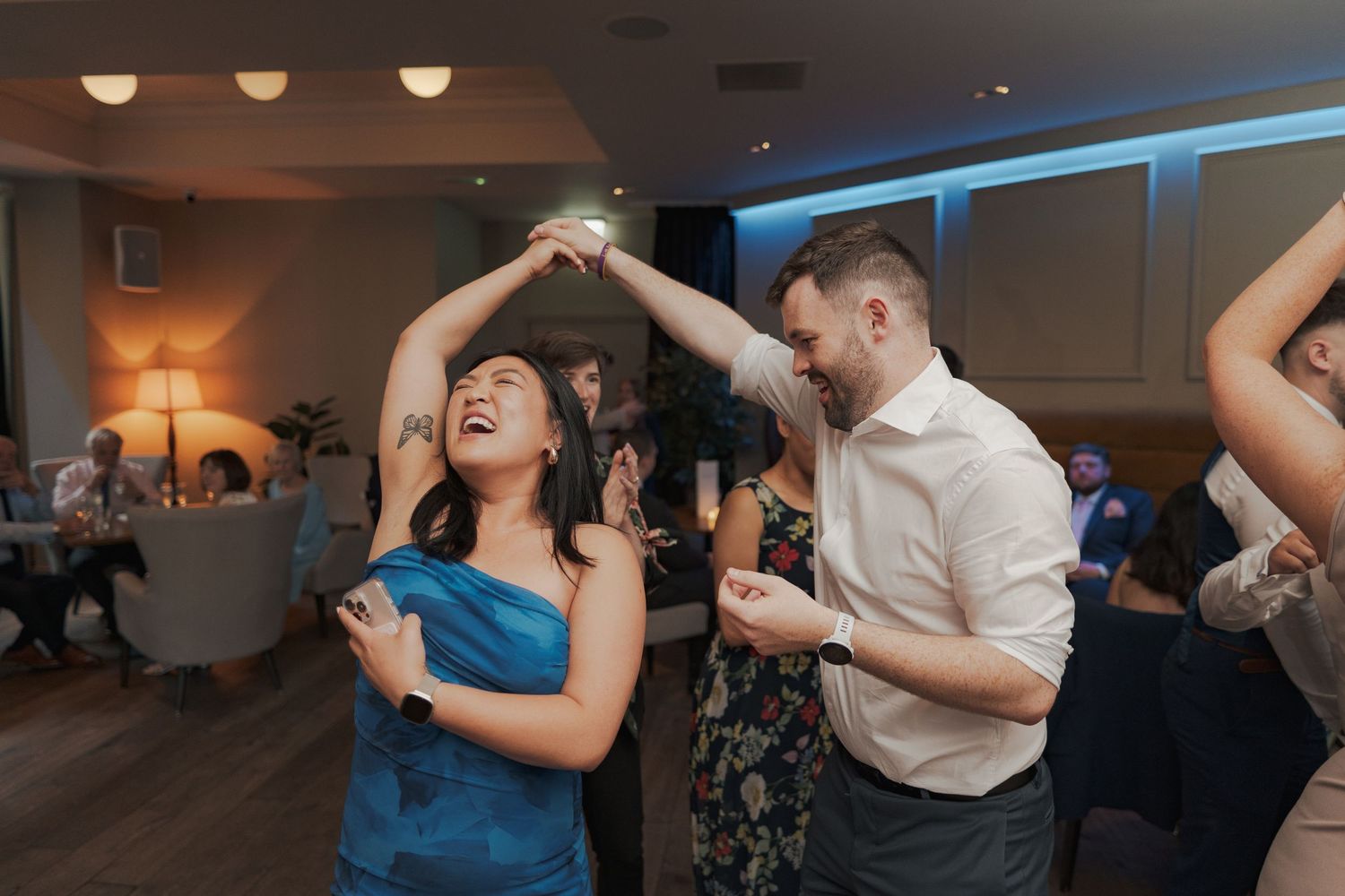 Wedding reception dance floor filled with guests dancing in a dimly lit venue with blue accent lighting at Citation Glasgow.