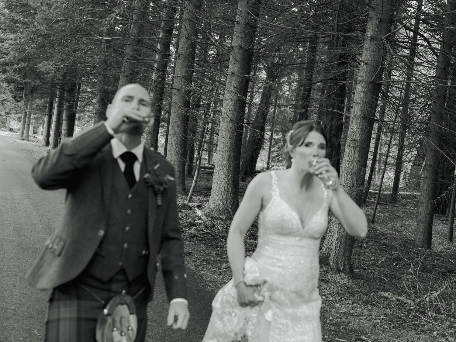 Black and white photo of a bride and groom drinking whisky in a Scottish forest wedding celebration.