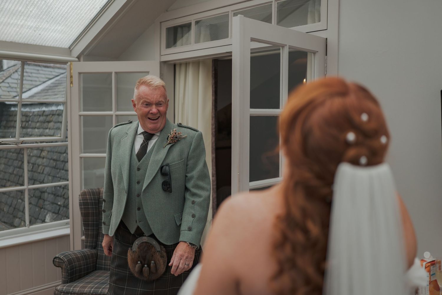A heartwarming first look wedding moment at a venue with glass windows and grey stone walls.