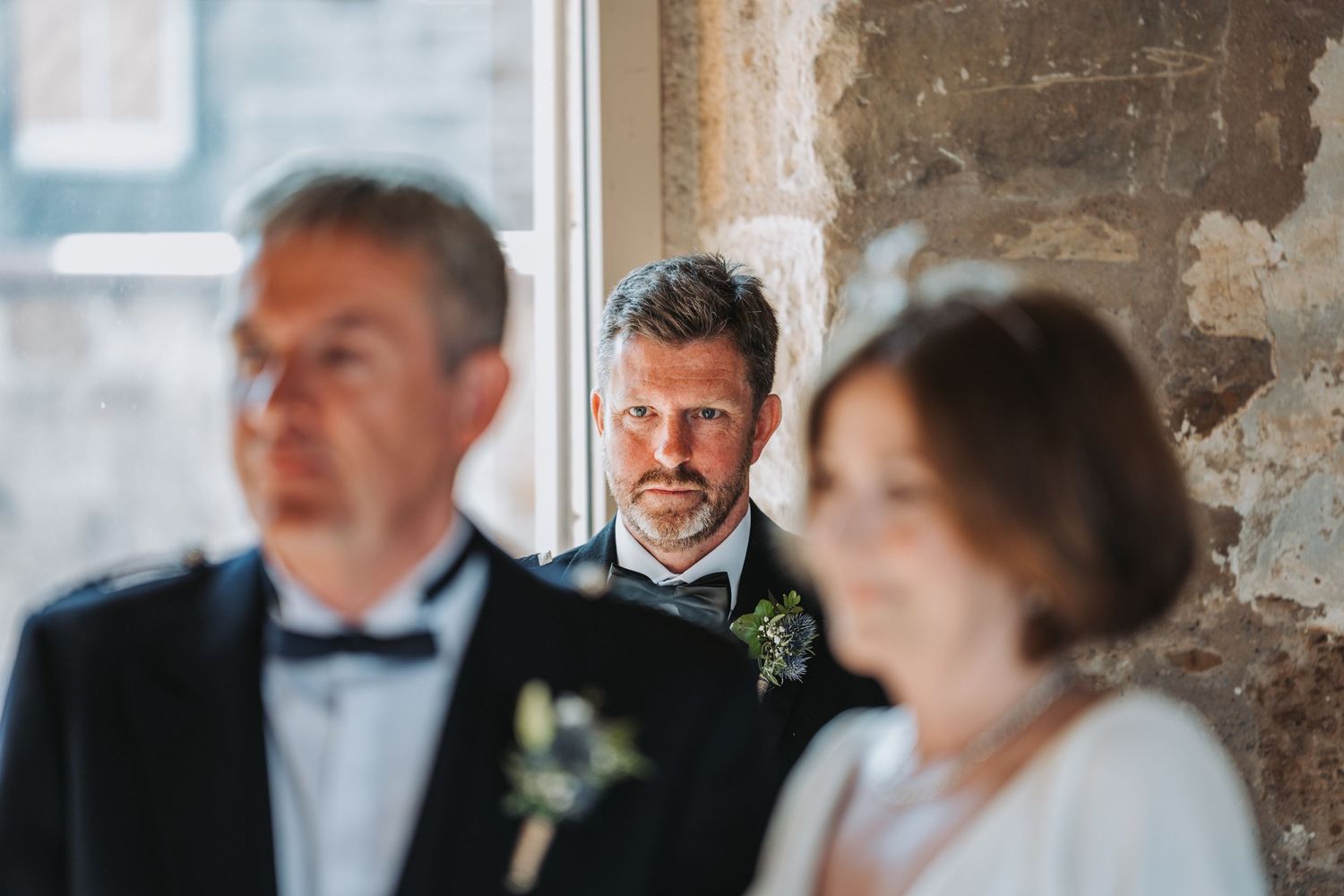 Elegantly dressed wedding party members in formal attire stand together in a rustic stone interior.