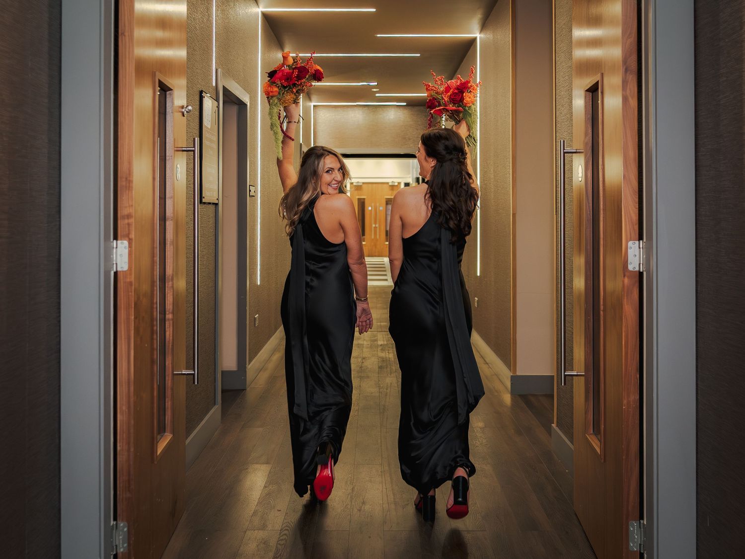 People in black outfits dance and move through a modern hallway with warm lighting and red decorative accents.
