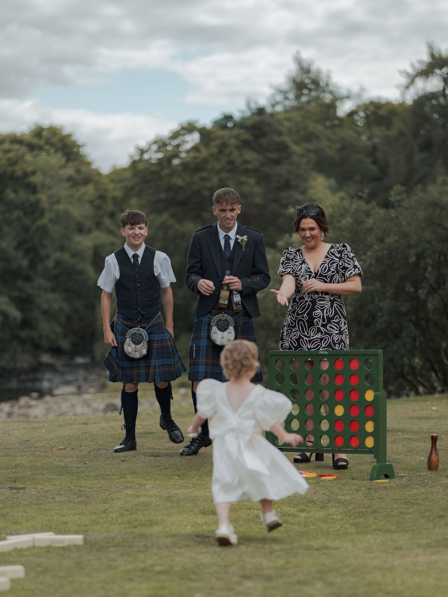 Wedding guests enjoying a game of giant Connect Four on a grassy lawn during an outdoor reception celebration.