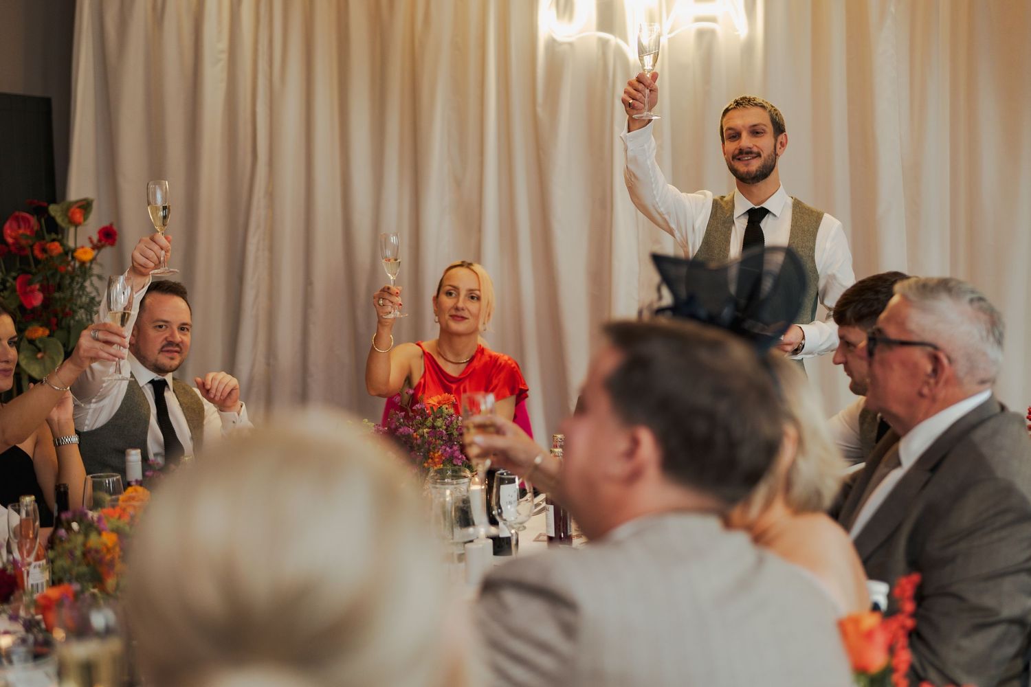 Wedding guests laugh and smile during a reception dinner under elegant chandelier lighting at the Sandman Signature, Aberdeen.