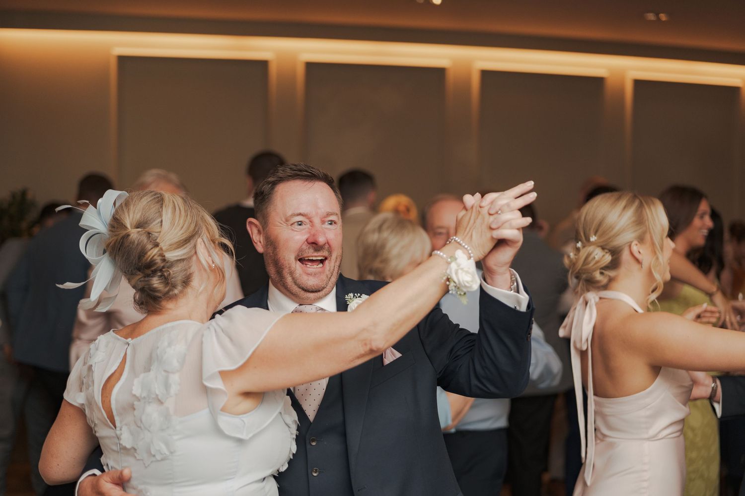 Wedding guests dance and celebrate together on a dimly lit dance floor during a reception celebration.