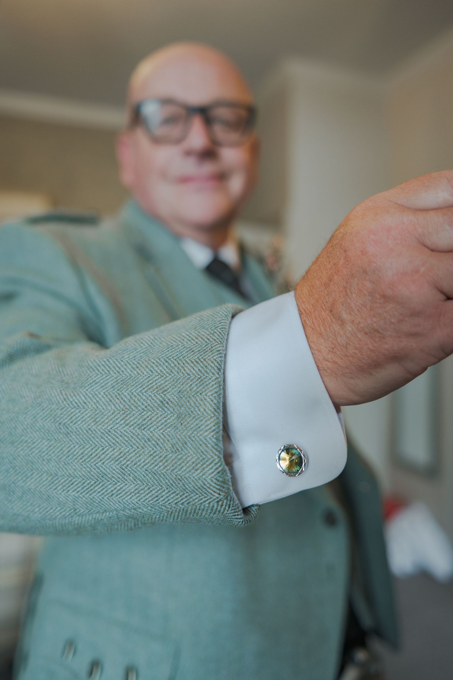 A close-up view of a dress shirt sleeve with cufflinks and a soft mint green sweater.