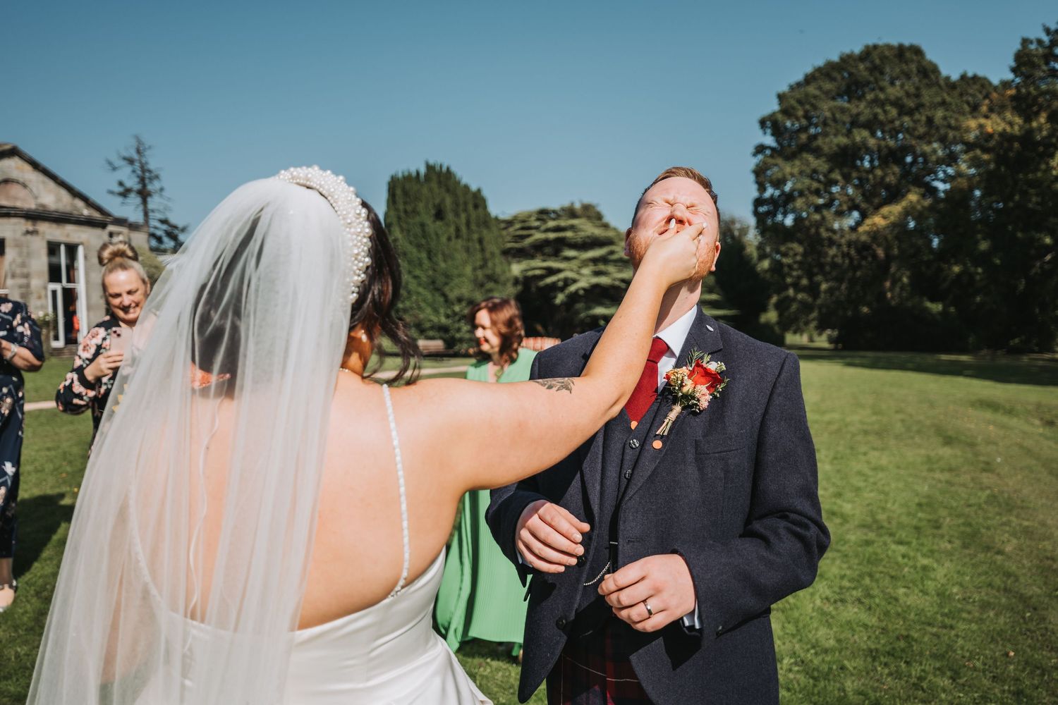 A joyful moment outdoors on a sunny wedding day as the couple shares a playful interaction on the lawn of Oswald House.
