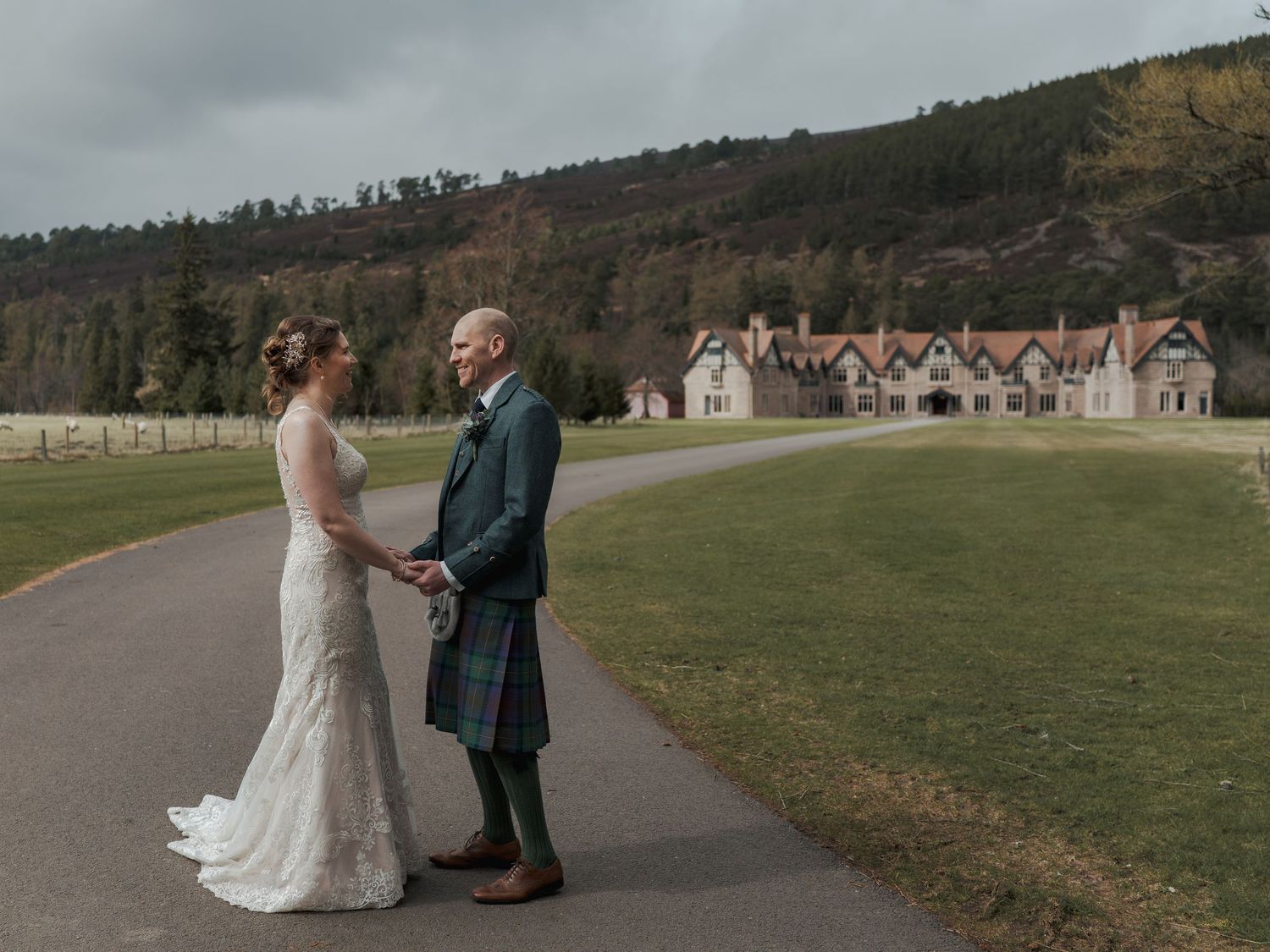 Bride and groom holding hands on a path at a Scottish Highland estate, groom wearing a tartan kilt.