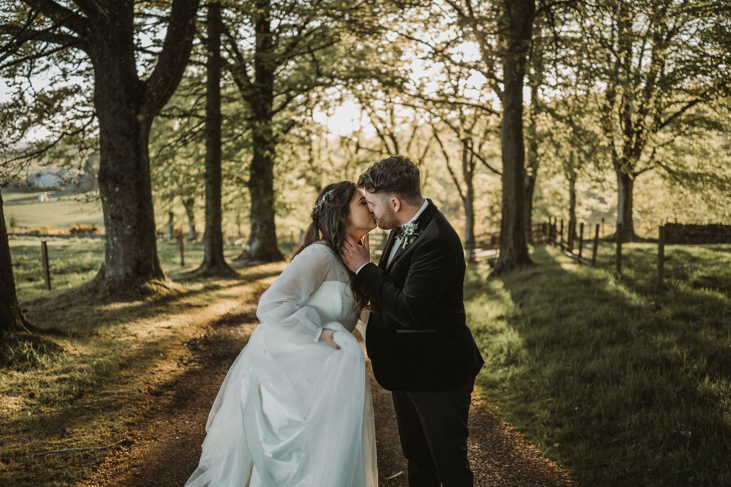 A wedding couple walks through a sunlit wooded park on a beautiful autumn day as golden light streams through trees.