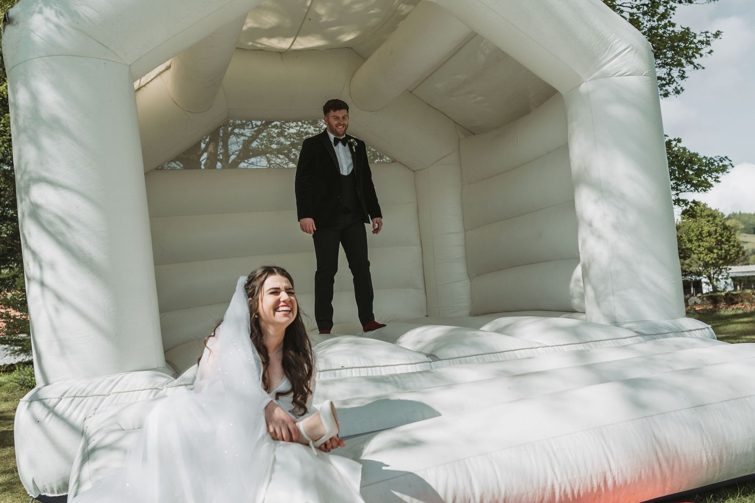 A bride and groom having fun on a white inflatable bounce house at their wedding celebration.