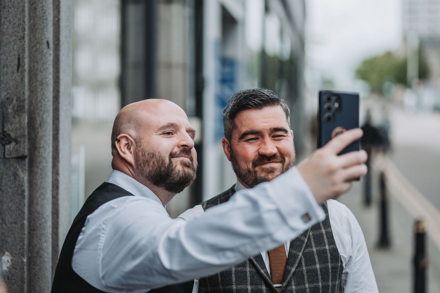 Two wedding guests in formal attire taking a selfie together outside.