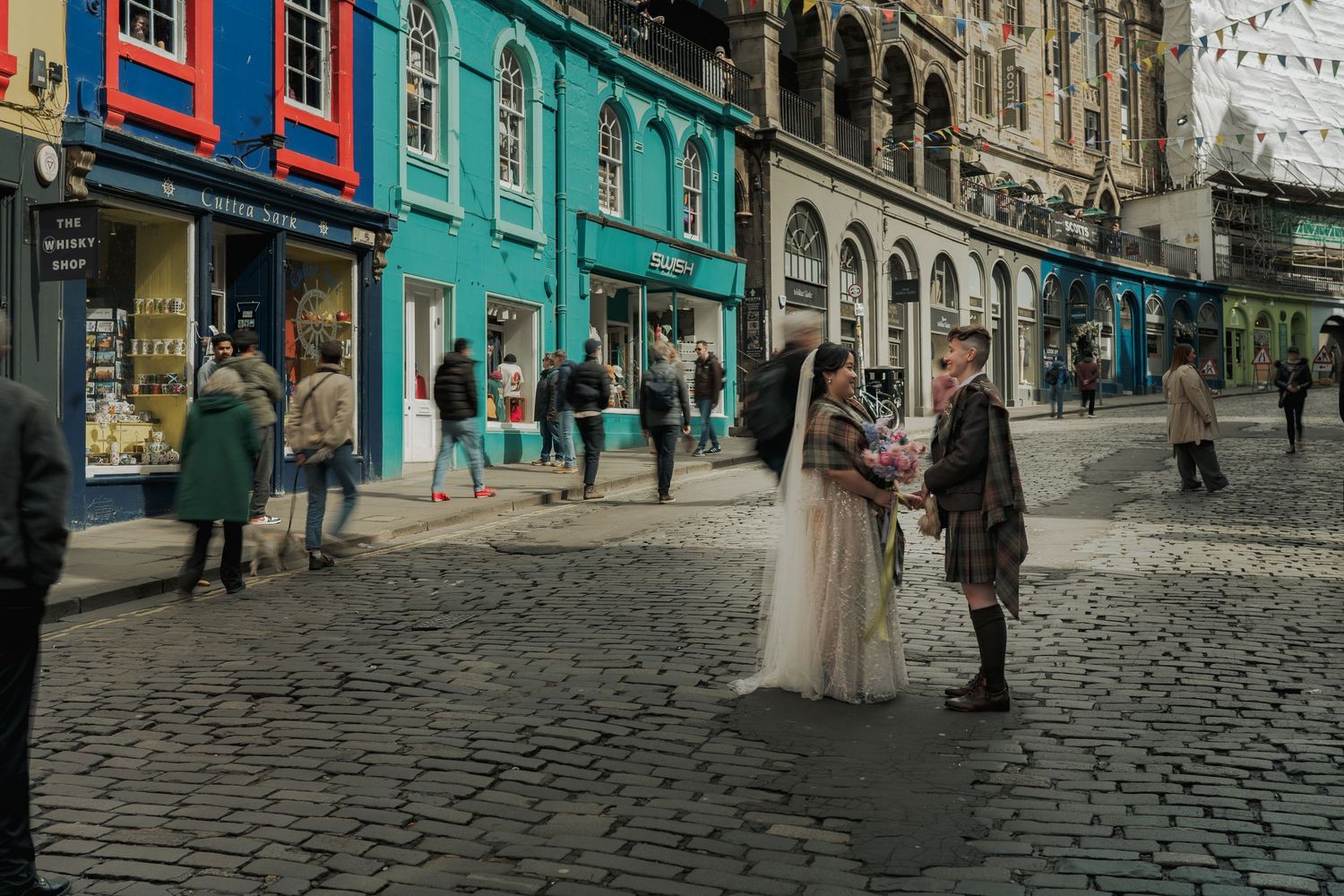 Bride and groom in traditional Scottish kilt pose on Victoria Street in colourful Edinburgh, Scotland.