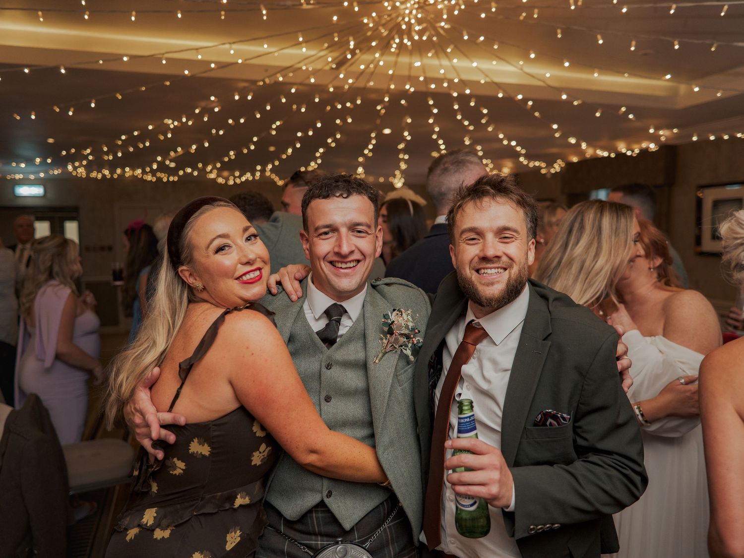 Wedding guests enjoying a lively dance party under romantic string lights during an indoor reception celebration at Banchory Lodge.