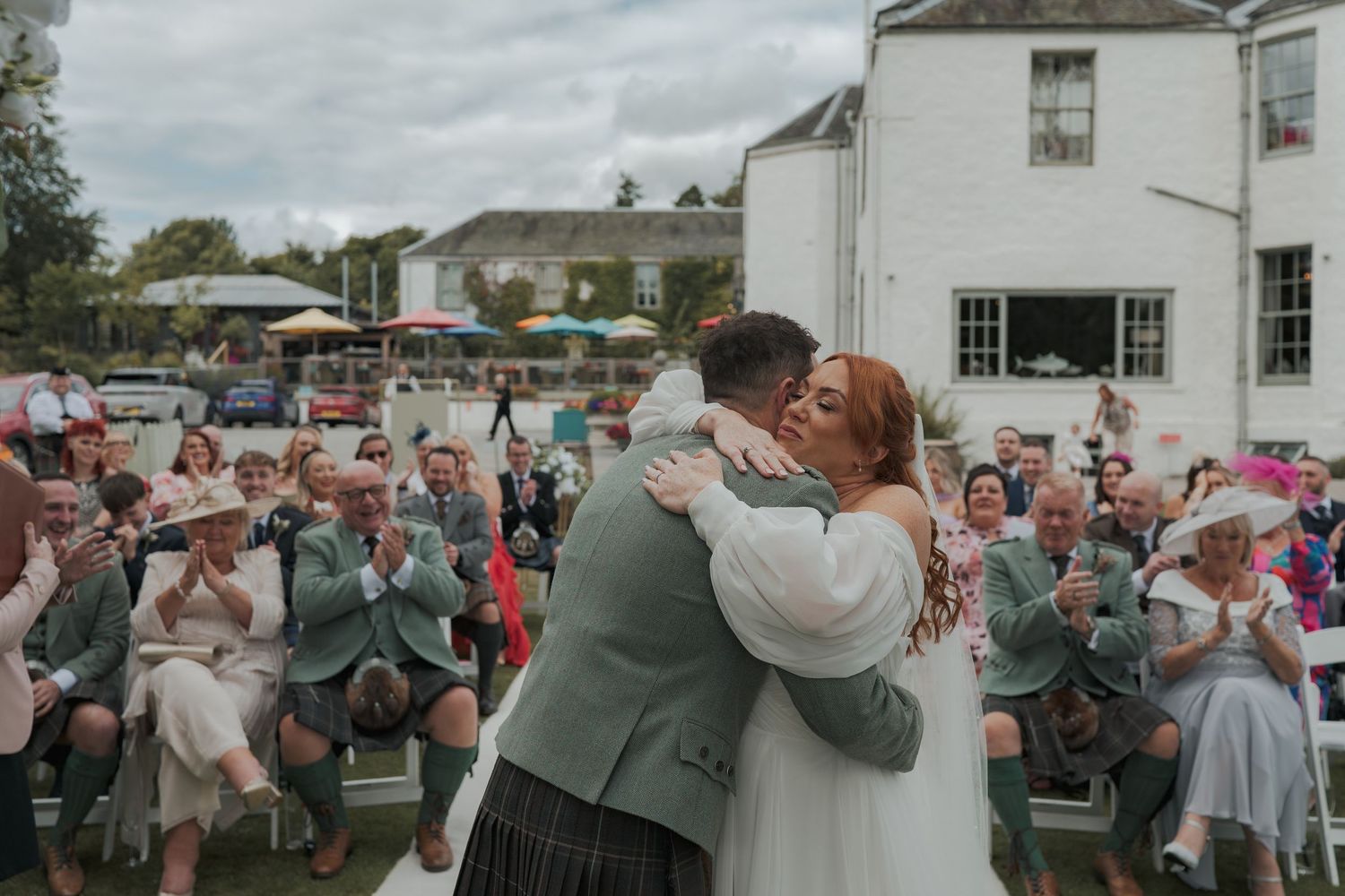 A group of people celebrate at a garden party dressed in festive attire with cups raised for a toast at Banchory Lodge.