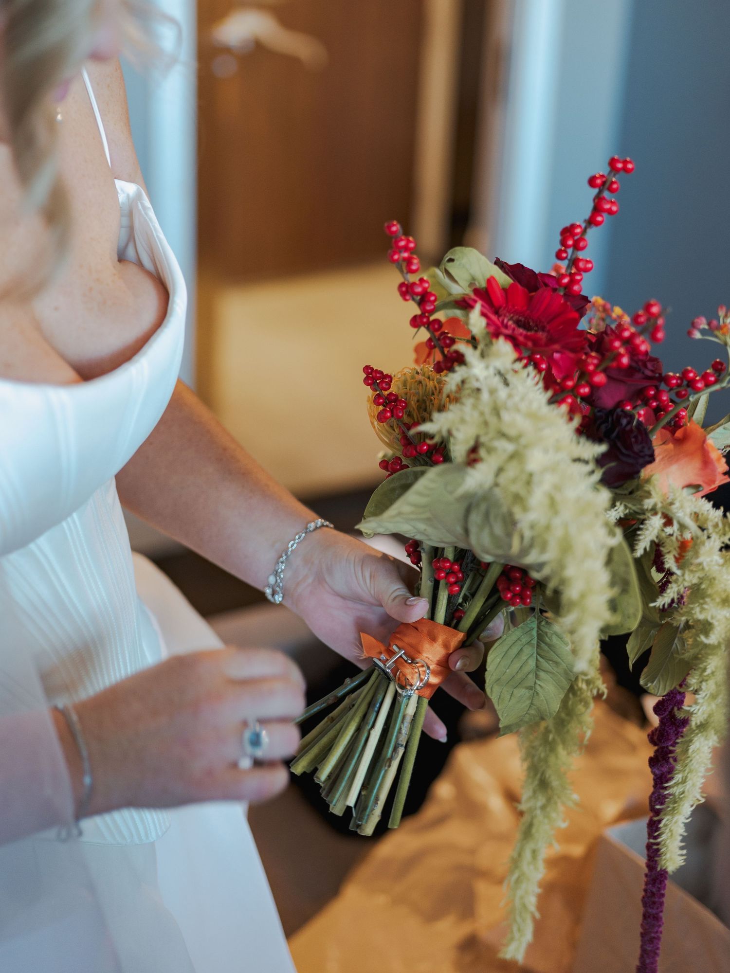 A bridal bouquet with white and red flowers is held against a white dress, showing a series of detail shots.