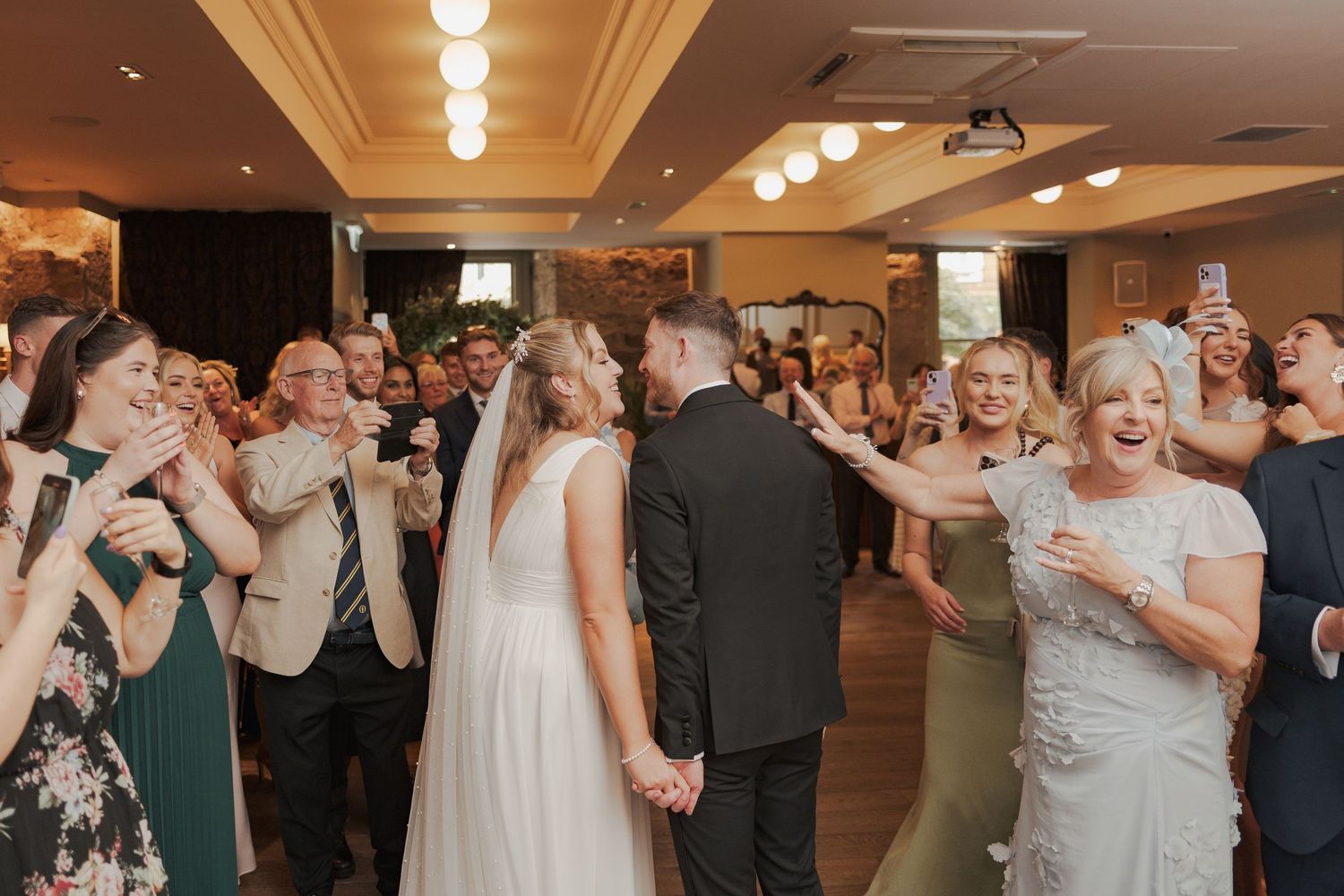 Wedding guests dance together in a circle during a lively reception celebration.