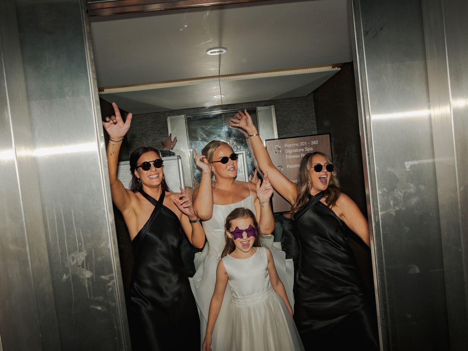 Wedding party celebrates in an elevator while wearing sunglasses and raising their hands in excitement at the Sandman Signature, Aberdeen.