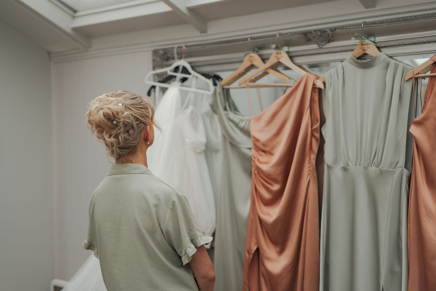Wedding dress fittings in a bridal boutique showing peach and sage colored bridesmaid dresses in a row.