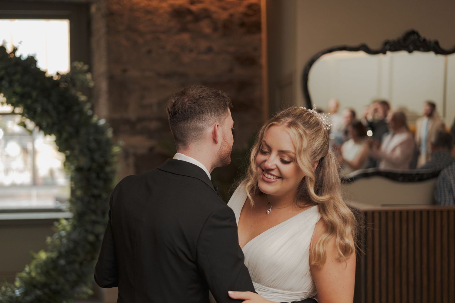 A couple shares an intimate moment during their wedding ceremony in a rustic indoor venue with greenery and vintage decor.