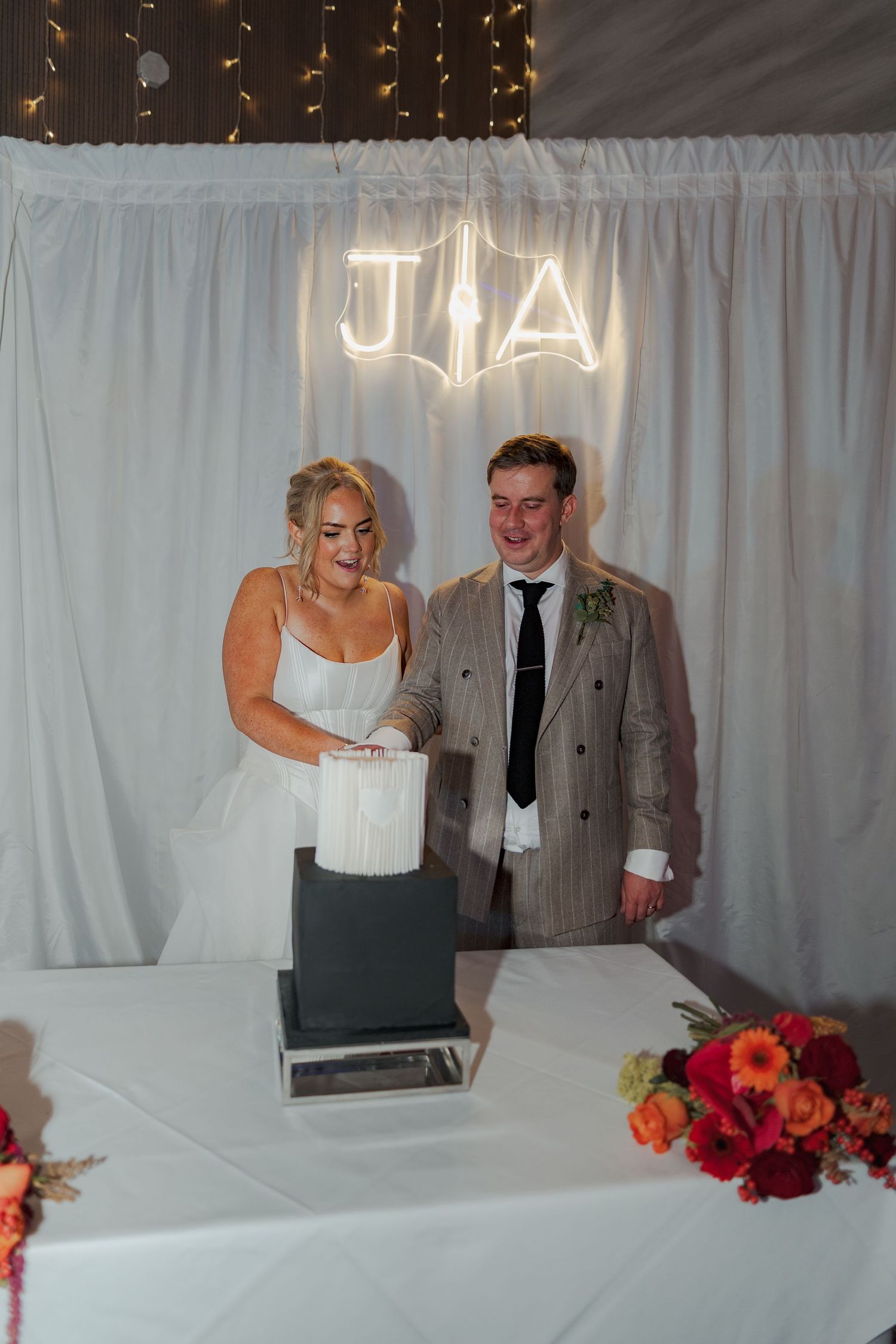 A couple shares a sweet moment at their wedding reception against a white curtain backdrop with red floral decor.