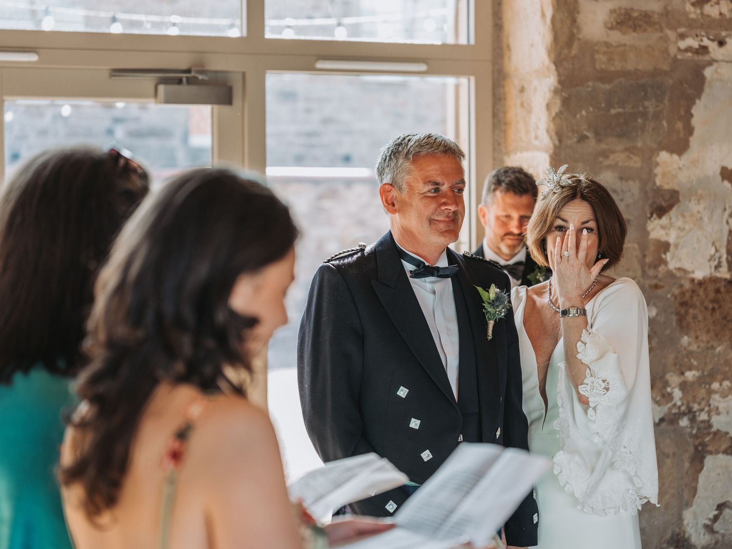 Wedding guests share a joyful moment during an indoor ceremony in Falside Mill with exposed brick walls.