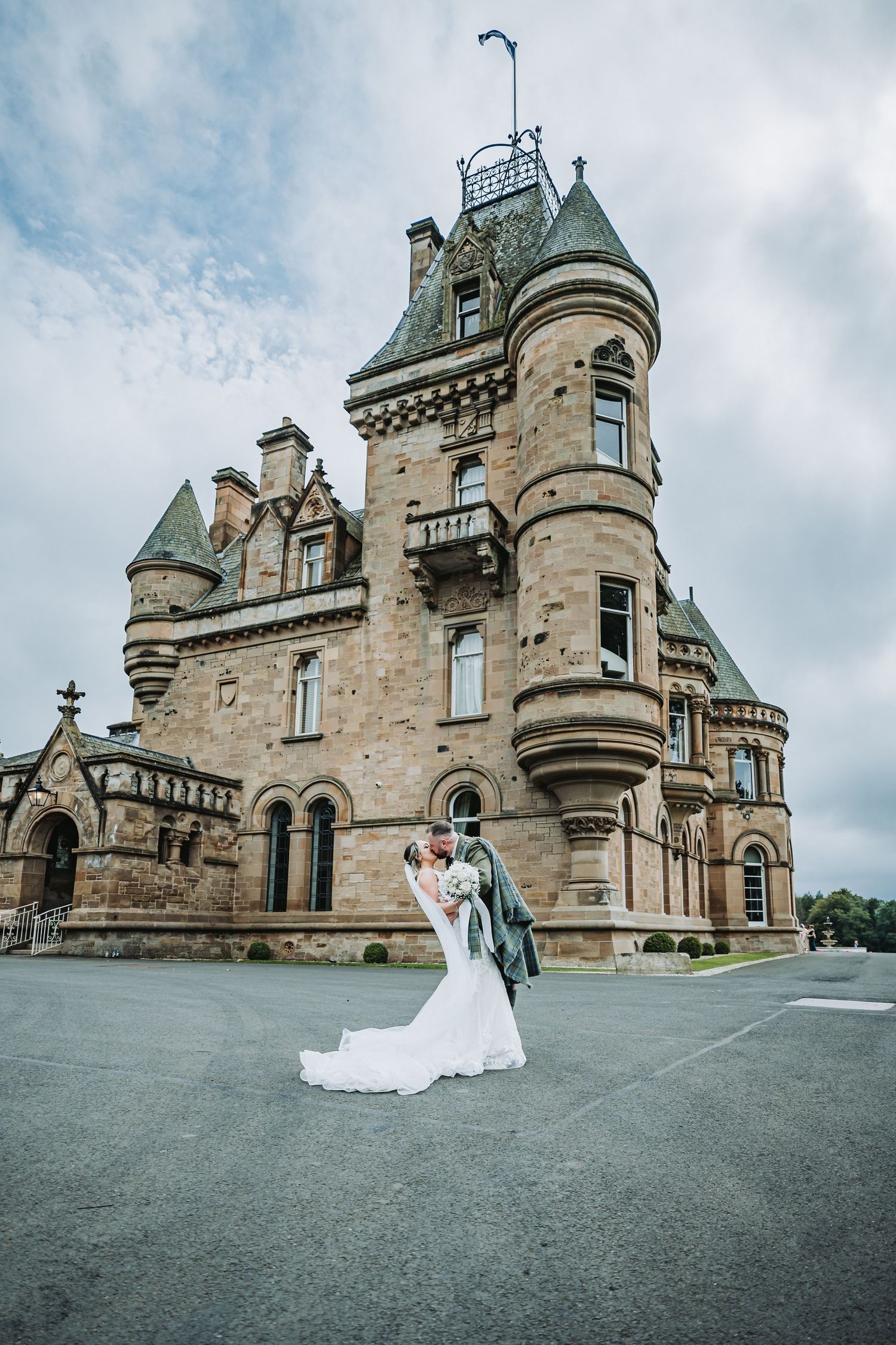 A romantic wedding couple poses in front of the majestic Cornhill Castle with turrets and stone architecture.