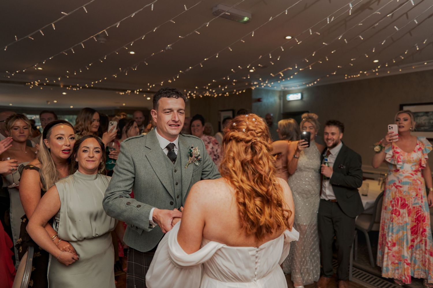 Wedding party enjoying a lively dance celebration with festive lighting and decor.