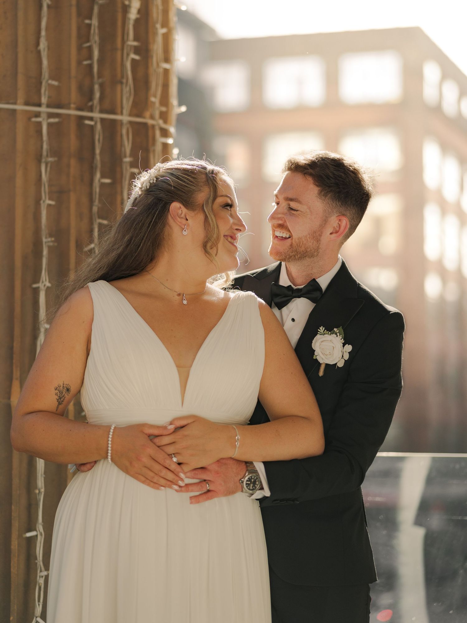 A couple shares an intimate moment at Citation Glasgow in formal attire against a sunlit backdrop with wooden beams.