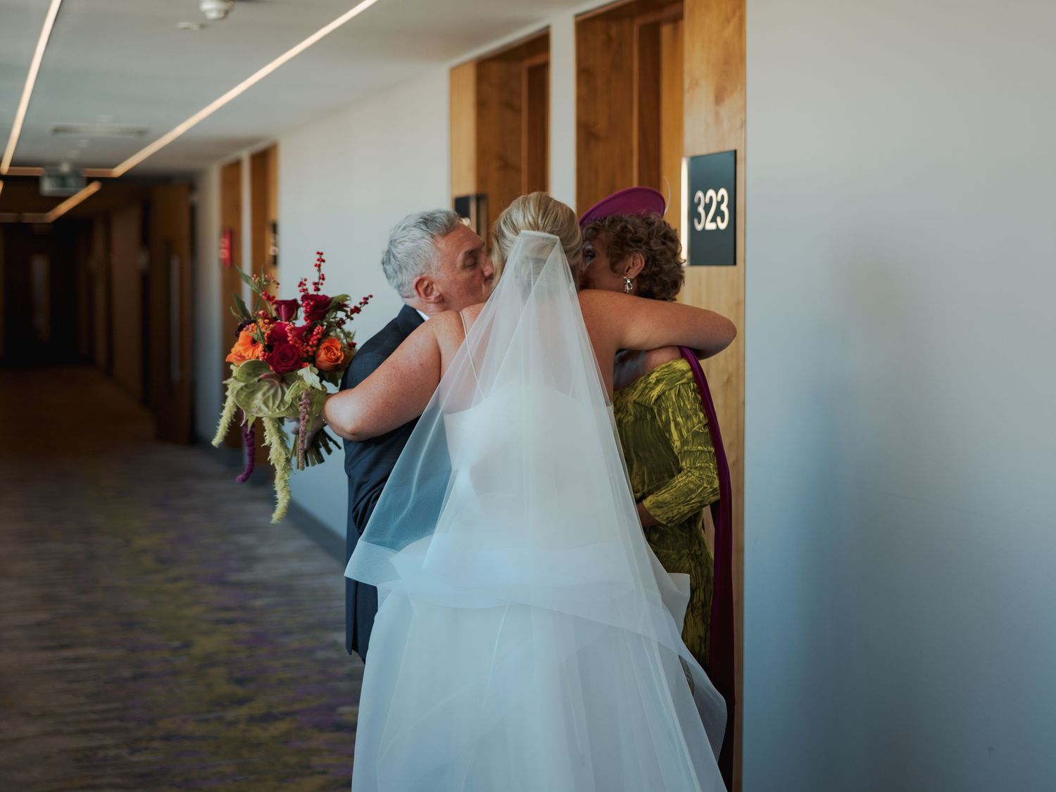 A bride in a flowing white gown walks down a modern hallway with natural lighting.