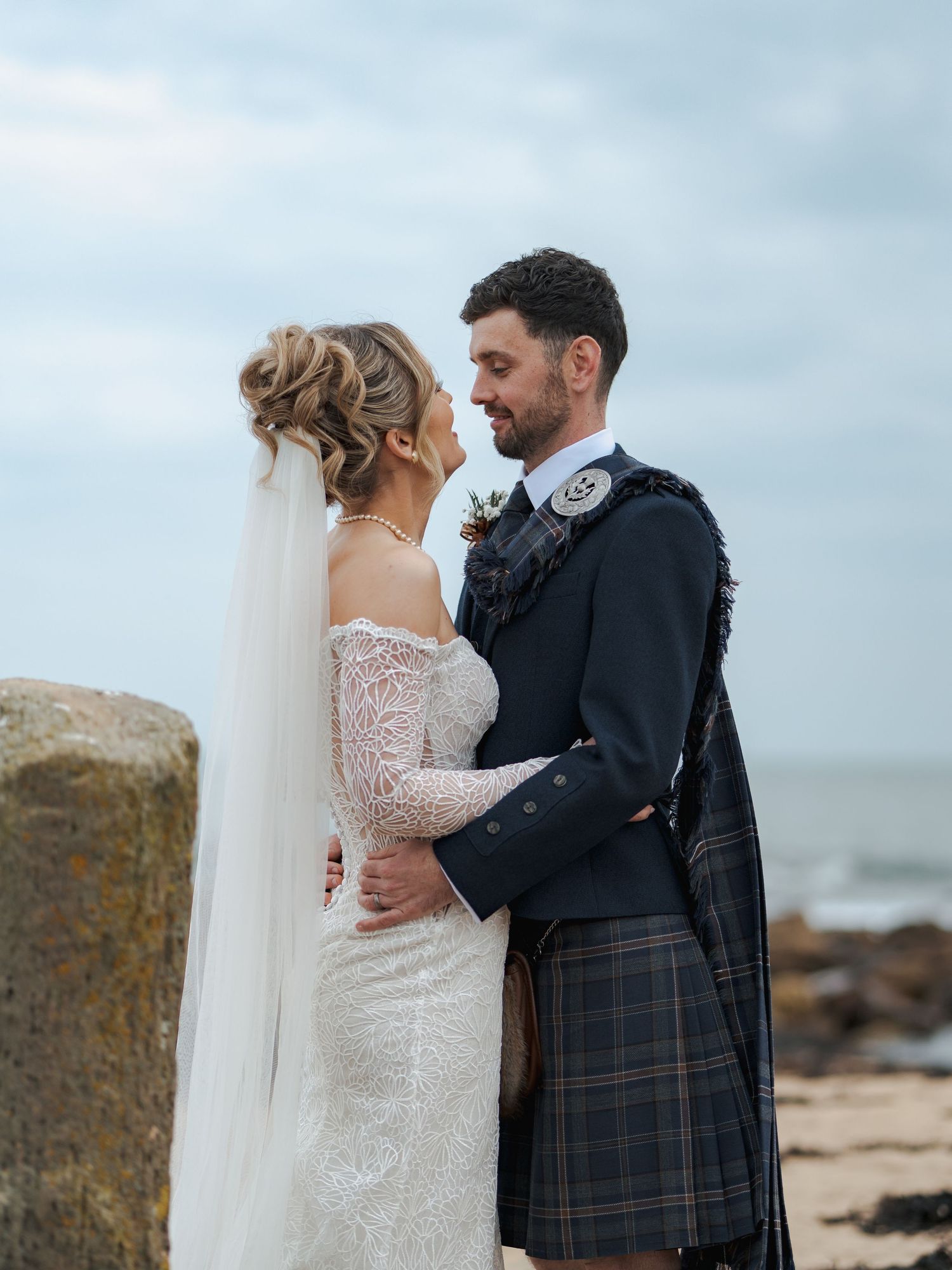 Newlywed couple shares intimate moments on a rocky beach during their Scottish wedding photoshoot.