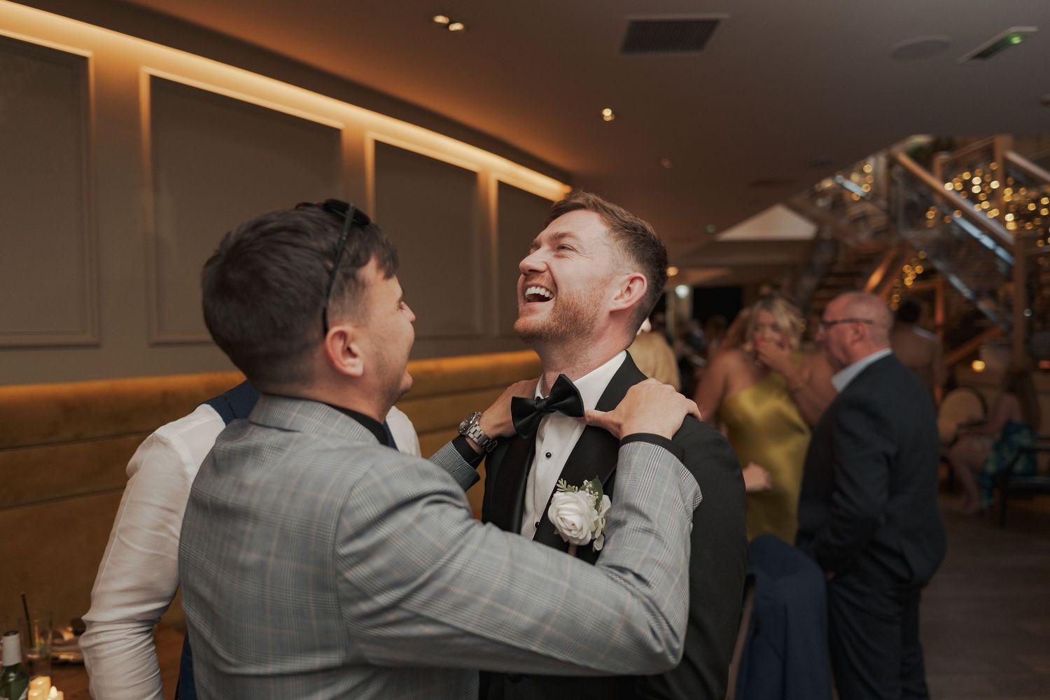 Couples dancing and laughing together at a wedding reception in a warmly lit indoor space.