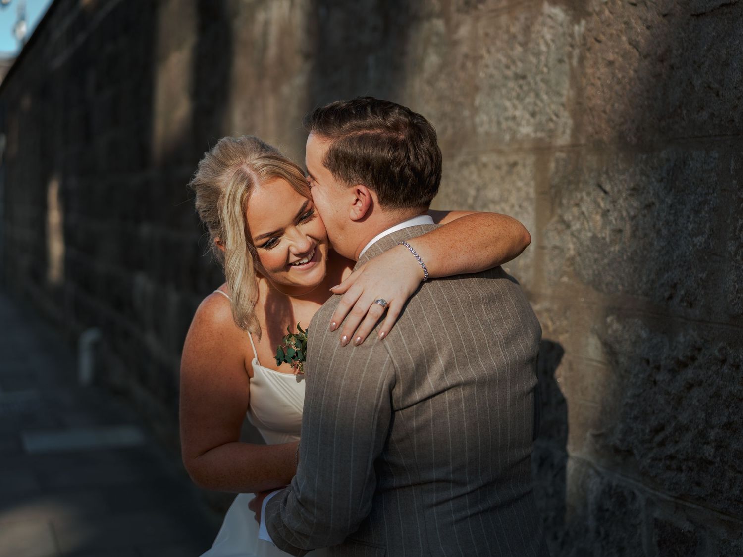 A romantic couple in wedding attire embraces and kisses in a stone archway at sunset at the Sandman Signature, Aberdeen.