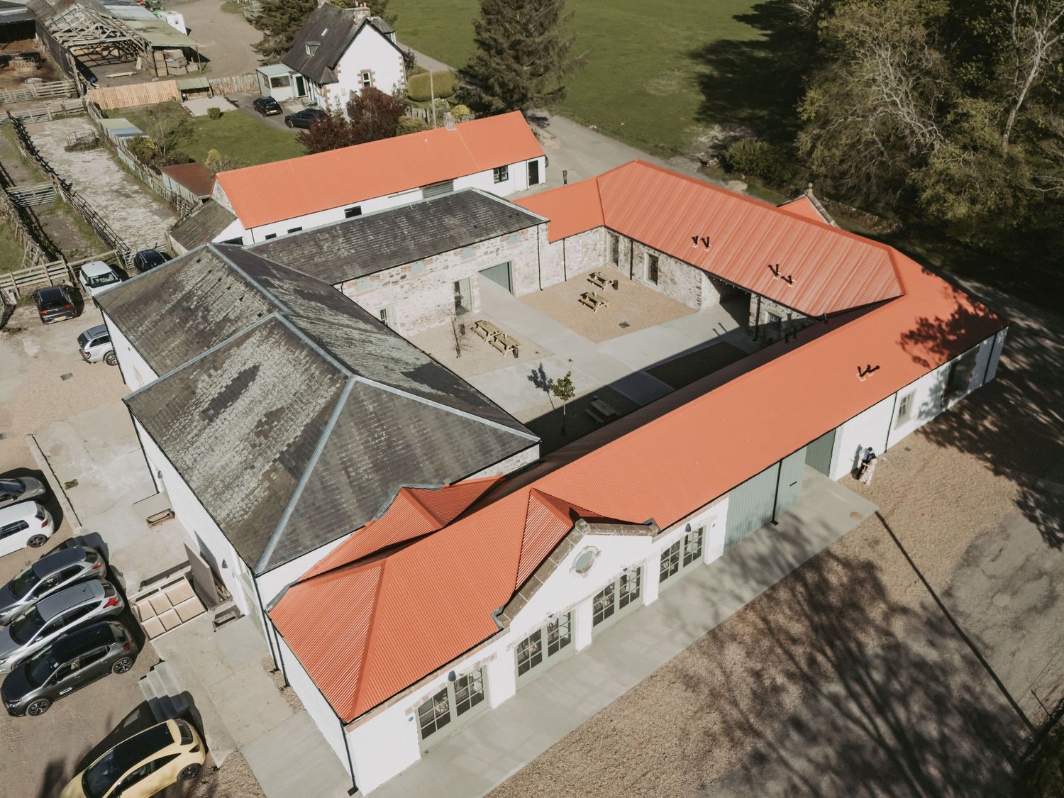 Aerial view of Kinclune Steading with red terracotta roofs and a glass atrium structure in the center courtyard.