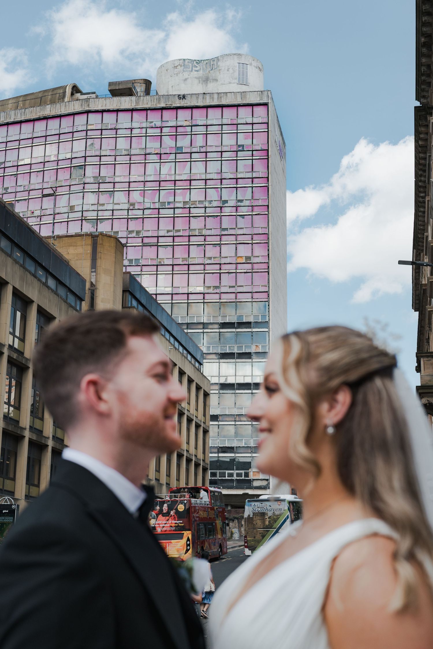 A couple shares a romantic moment outside a modern glass office building with pink geometric patterns.