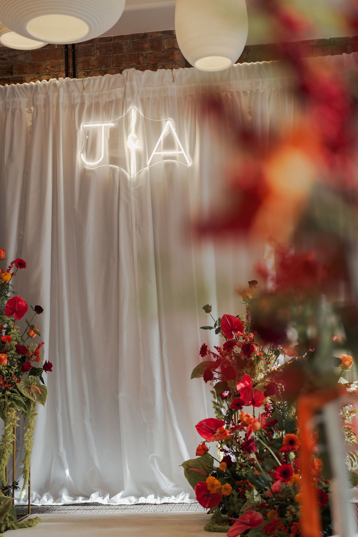 White curtain backdrop decorated with vibrant red and orange floral arrangements for an event at the Sandman Signature, Aberdeen.