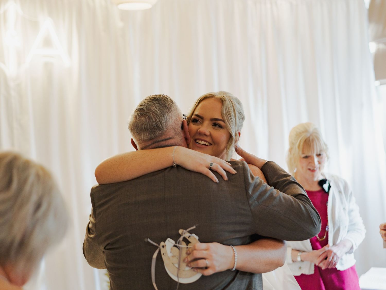 Emotional embraces shared between guests at a wedding reception with white curtain backdrop.