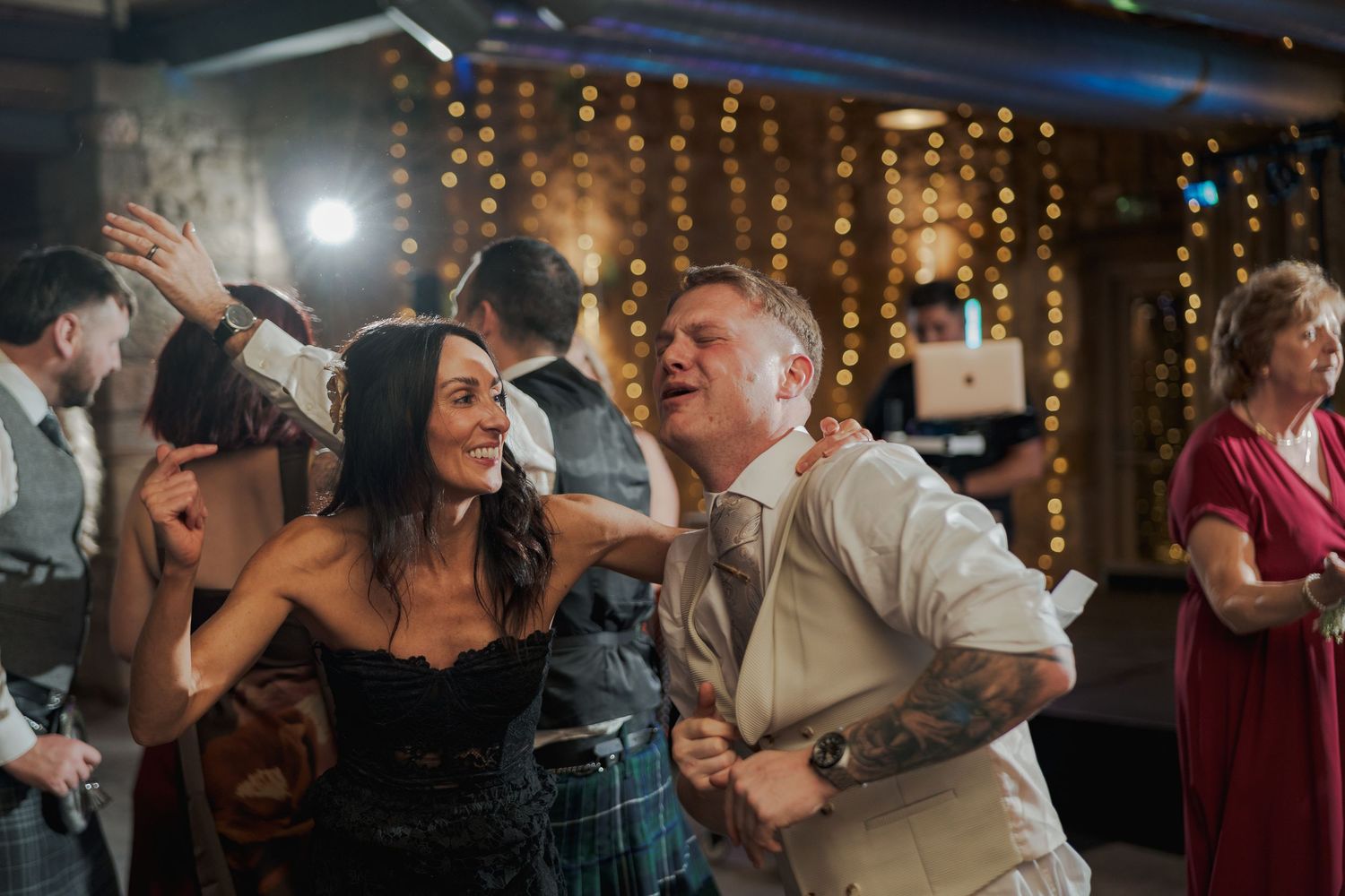 Wedding celebration at Falside Mill with guests dancing under romantic string light decorations.